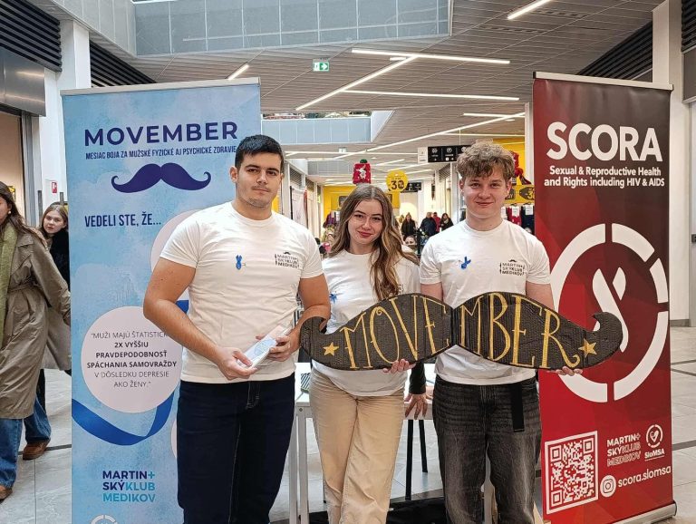Dobrovoľníci SCORA s nápisom Movember pri stánku v obchodnom centre